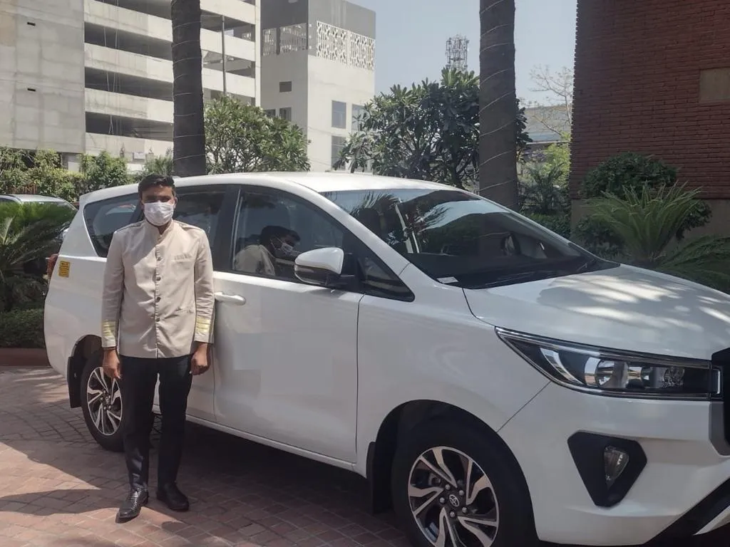 Pal Tour chauffeur in uniform beside a white Toyota Innova, ready for a cab booking in Delhi